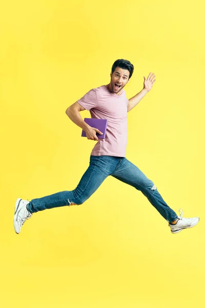Glücklich aufgeregter Mann mit Buch springt auf gelbem Hintergrund — Stockfoto