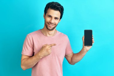 Mavi arka planda cep telefonuna işaret eden gülümseyen adamın portresi
