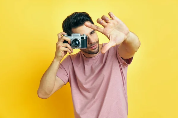 Schöner Mann fotografiert mit Retro-Kamera auf gelbem Hintergrund — Stockfoto