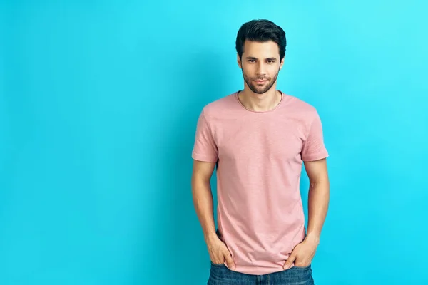 Junger gutaussehender Mann im rosafarbenen T-Shirt mit Blick in die Kamera auf blauem Hintergrund — Stockfoto