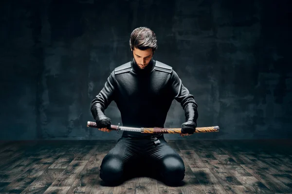 Krijger man zittend op de vloer poserend met een zwaard — Stockfoto