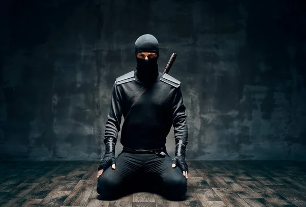 Ninja diz çöküp siyah arka planda kılıçla poz veriyor. — Stok fotoğraf