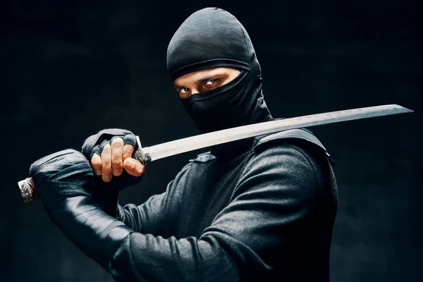 Kämpfende Ninja posieren mit einem Schwert über schwarzem Hintergrund — Stockfoto