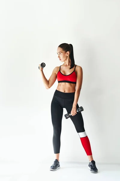 Deportiva mujer en ropa deportiva haciendo ejercicio con pesas sobre fondo blanco. —  Fotos de Stock