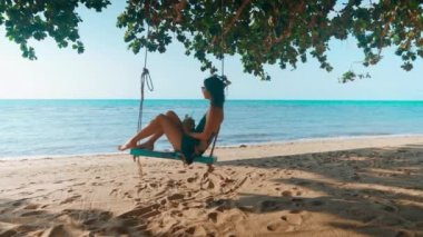 Kaygısız genç kadın salıncakta rahatla, hindistan cevizi suyu iç ve denizin tadını çıkar.