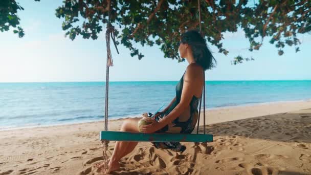 Беззаботная счастливая женщина на качелях отдыхает и наслаждается морем на тропическом пляже — стоковое видео