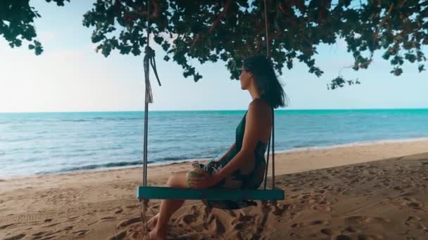 Беззаботная счастливая женщина на качелях отдыхает и наслаждается морем на тропическом пляже — стоковое видео