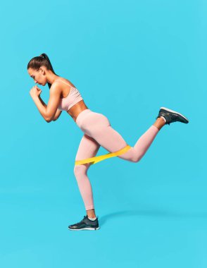 Mavi arka planda direnç bandı ilmek egzersizleri yapan sportif kadın.