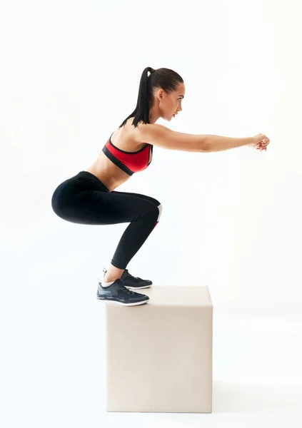 Deportiva mujer practicando ejercicios en cuclillas con gran cubo sobre fondo blanco — Foto de Stock