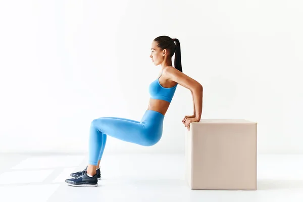 Deportiva mujer practicando ejercicios en cuclillas con gran cubo sobre fondo blanco. —  Fotos de Stock