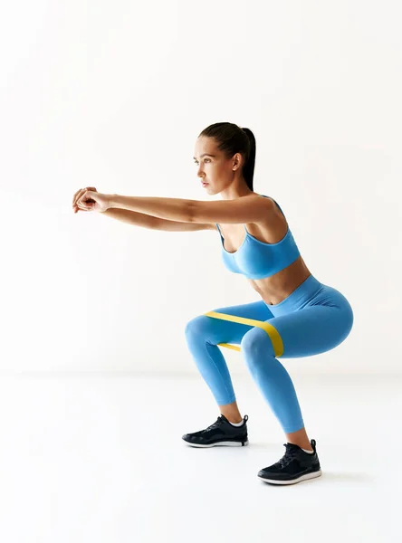 Mujer deportiva practicando ejercicios en cuclillas con bucle de banda de resistencia sobre fondo blanco —  Fotos de Stock