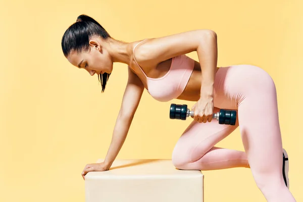 Joven mujer deportiva en ropa deportiva haciendo ejercicio con mancuernas sobre fondo amarillo —  Fotos de Stock