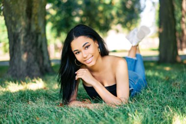 Güzel gülümseyen afro-amerikalı kadın parkta dinleniyor yeşil çimlerde yatıyor.