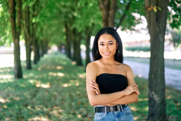 Lächelnde selbstbewusste Afroamerikanerin mit verschränkten Armen posiert draußen — Stockfoto