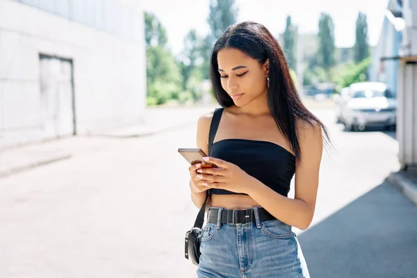 Mooie zwarte vrouw op zoek naar haar mobiele telefoon lopen in de stad — Stockfoto