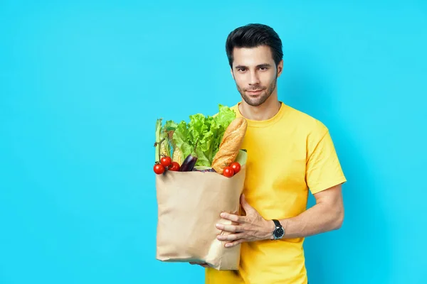 Young handsome man holding paper shopping bag full of fresh vegetables