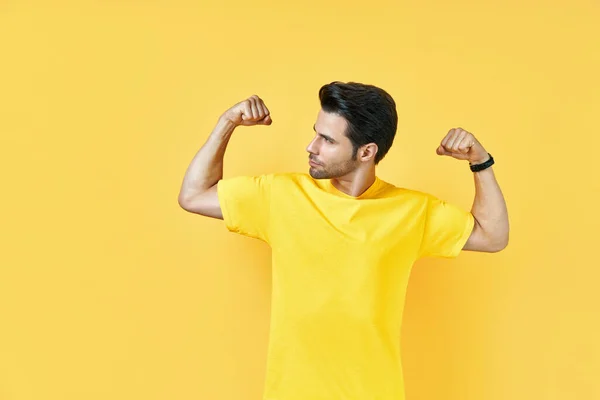 Hombre musculoso guapo muestra músculos en sus brazos sobre fondo amarillo — Foto de Stock