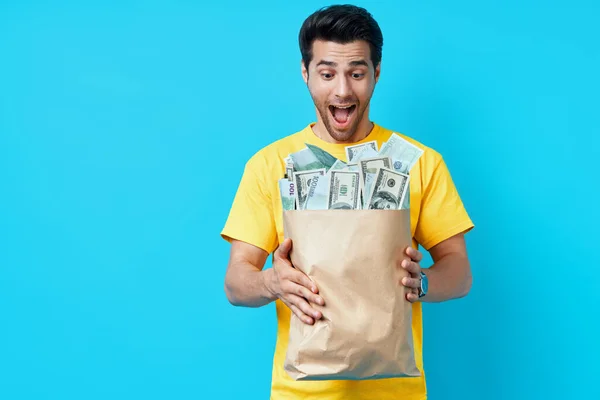 Spännande glad man hålla papperspåse full av högar med pengar isolerade på blå bakgrund. — Stockfoto