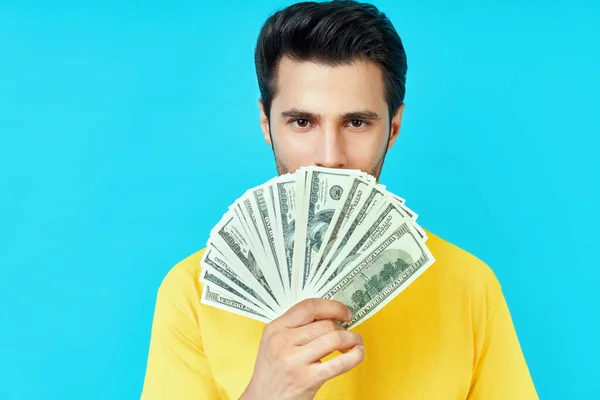 Glad ung man håller stack med pengar och skryta med sina besparingar på blå bakgrund — Stockfoto