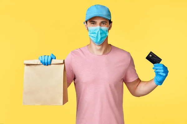 Szállítási ember tartsa papír csomag élelmiszer-és hitelkártya visel arc maszk és kesztyű, mint a védelem COVID-19 — Stock Fotó