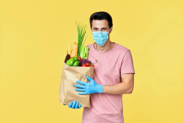 Férfi tartó papír bevásárló táska tele friss zöldségekkel visel arc maszk és kesztyű védelmében COVID-19 — Stock Fotó