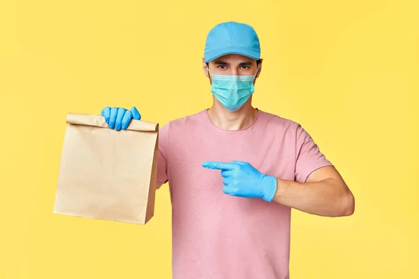 Entrega hombre apuntando en paquete de papel con comida usando mascarilla y guantes —  Fotos de Stock