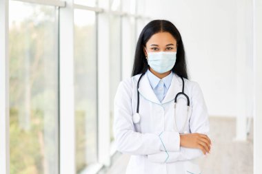 Hastane geçmişinde kolları çaprazlanmış tıbbi maske takan kadın doktor.