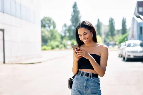 Šťastný úsměv černošky žena při pohledu na její smartphone procházky ve městě — Stock fotografie