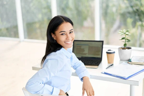 Glimlachende jonge Afro-Amerikaanse zakenvrouw poseren aan haar bureau in een helder modern kantoor — Stockfoto