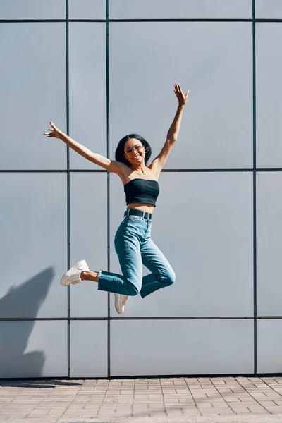 Retrato de alegre positivo preto menina pulando no ar na parede rua fundo — Fotografia de Stock