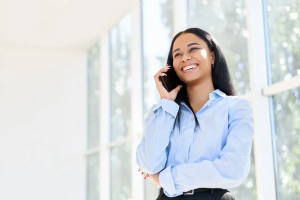 Glimlachende Afro-Amerikaanse zakenvrouw aan de telefoon in open ruimte modern kantoor — Stockfoto