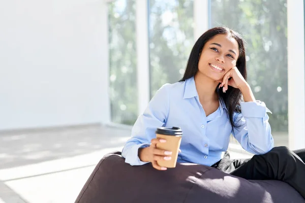 Sonriente mujer de negocios bastante negro relajarse con la taza de café en la mano durante el tiempo de descanso en la oficina moderna — Foto de Stock