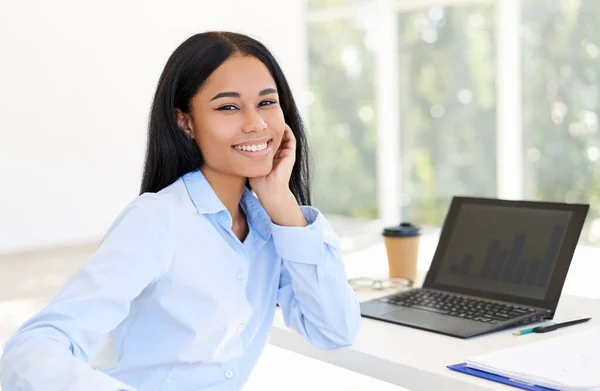 Glückliche schwarze Geschäftsfrau posiert an ihrem Schreibtisch in einem hellen modernen Büro — Stockfoto