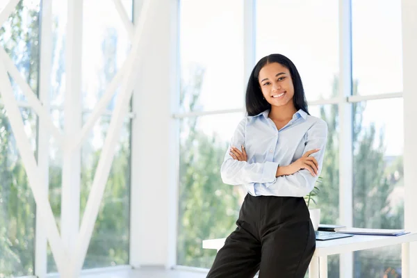 Lachend zelfverzekerde zwarte zakenvrouw poserend in een modern kantoor met gekruiste armen — Stockfoto