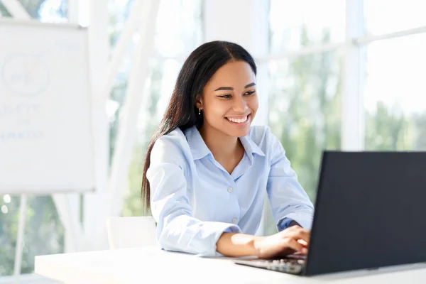 アフリカ系アメリカ人のビジネスマンの笑顔仕事上のラップトップ座って彼女の机で現代オフィス — ストック写真
