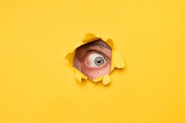 Yırtık sarı kağıttan kameraya bakan insan gözünün yakın çekimi