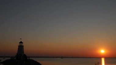 Deniz feneri insan siluetleri ile çevresinde, Yelkenli teknelerle okyanusta büyük bir yuvarlak güneş ayarlar 