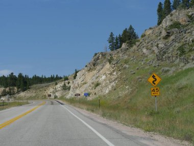 Wyoming Bighorn Ulusal Ormanı'nda bir tepenin eteklerinde yol kenarında küçük yönlü ve hız sınırı işaretleri Satır.