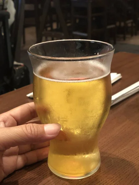 テーブルの中で冷たいビールのグラスを持つ手 — ストック写真