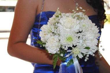 Gelinin hizmetçisi elinde bir buket beyaz kasımpatı çiçeği tutuyor. 