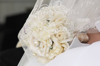 Bir demet beyaz gül ve incinin dantel bir peçenin altında yan görüntüsü.