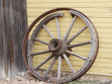 Tahta bir duvara dayanmış kırık ahşap telleri olan kırık bir arabanın tekerleği.