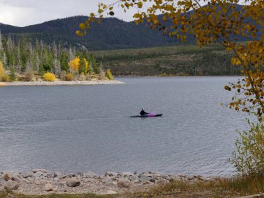 Dillon Gölü ya da Dillon Reservoir 'ın çerçeveli manzarası. Sonbaharın güzel bir gününde mor bir kanoyla kürek çeken bir kadın.. 