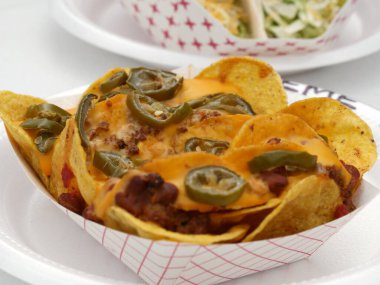 Jalapeno, et ve erimiş peynirle dolu kağıt tabakta nacho. 