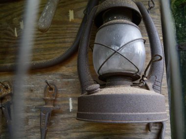 Duvarda asılı antika paslı bir gaz lambası ve diğer paslı aletlerle birlikte bir çiftlik evinde.