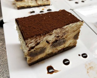 Üzerinde çikolata tozu olan bir dilim vanilyalı pasta ve bir damla çikolata şurubu.