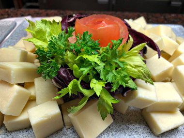 Dilimlenmiş domates ve yeşilliklerle süslenmiş Edam peyniri küplerini kapatın.