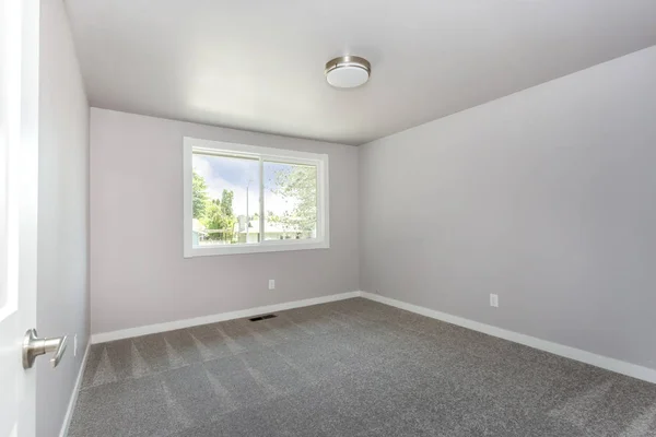 Small empty room with a window and grey carpet floor.