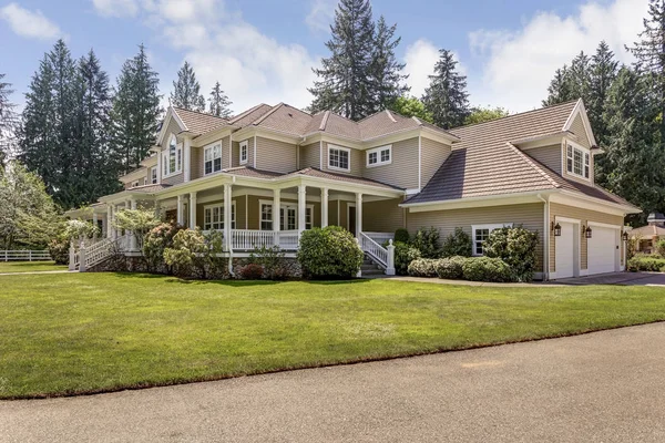 Exterior view of a large country home with covered deck and beautiful green landscape.