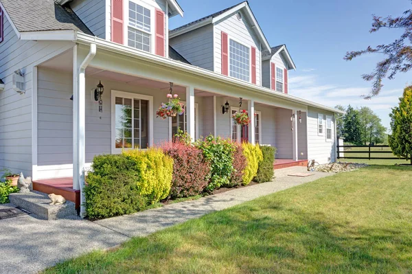 Nice home showcases a cozy covered porch with red front door and well kept lawn in the front yard on a bright summer day.